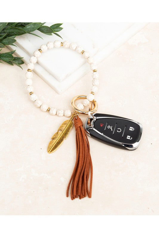 A Boho Stone Key Ring Bracelet with a suede tassel and charm keychain on a person's wrist, with a car key attached.