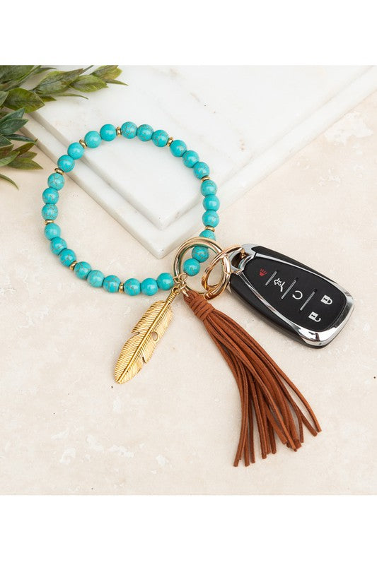A Boho Stone Key Ring Bracelet with a suede tassel and charm keychain on a person's wrist, with a car key attached.