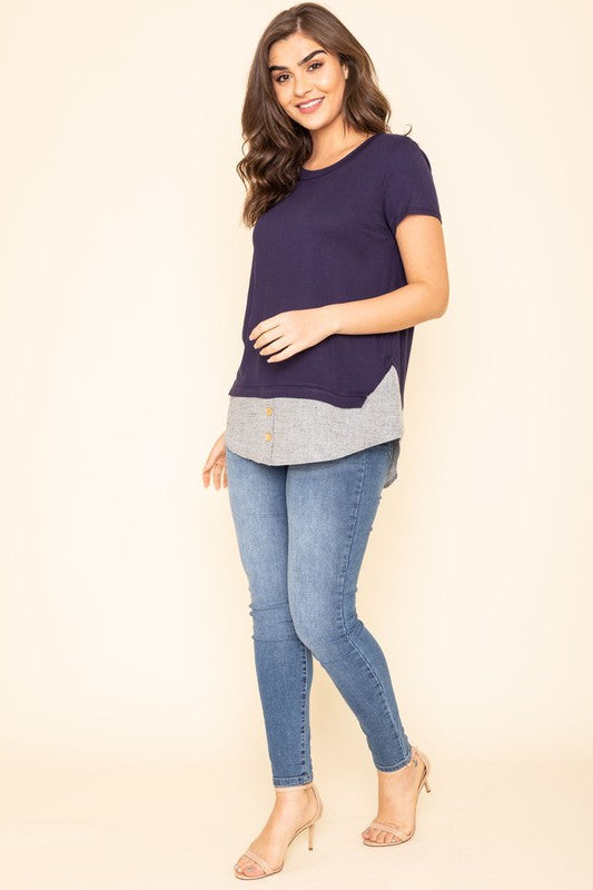 A woman wearing a Short Sleeve Layered Top stands against a beige background, highlighting the simplicity and comfort of this grey T-shirt with blue trim at the bottom, proudly made in the United States.