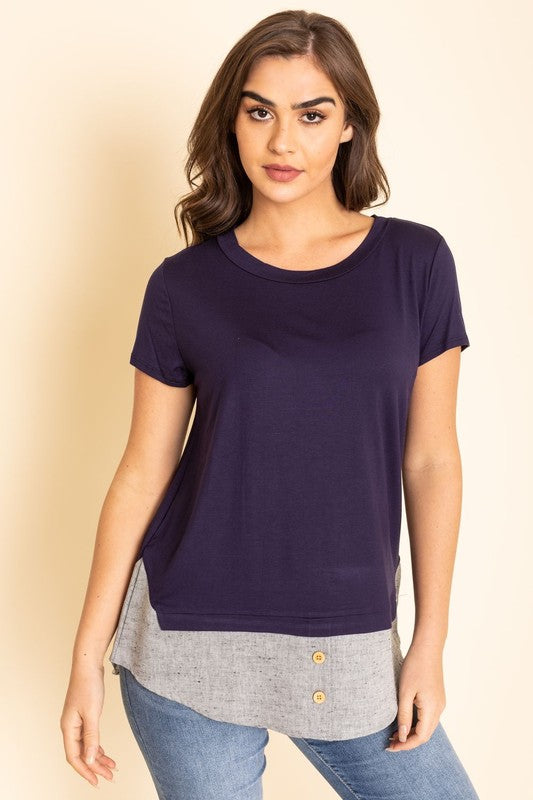 A woman wearing a Short Sleeve Layered Top stands against a beige background, highlighting the simplicity and comfort of this grey T-shirt with blue trim at the bottom, proudly made in the United States.