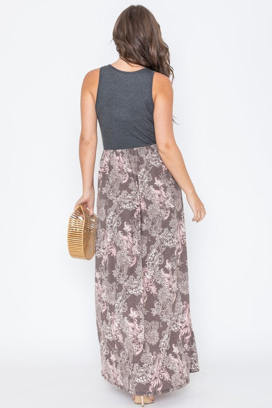 A woman wearing a Plus Sleeveless Paisley Maxi Dress is holding a wooden handbag and smiling.