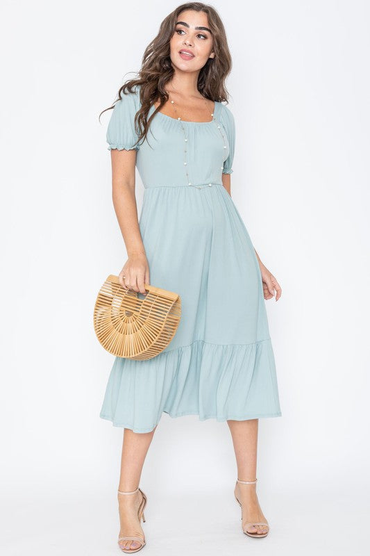 A woman in a Square Neck Puff Sleeve Boho Dress in light blue holds a wooden handbag. She stands on a plain background, wearing strappy heels.