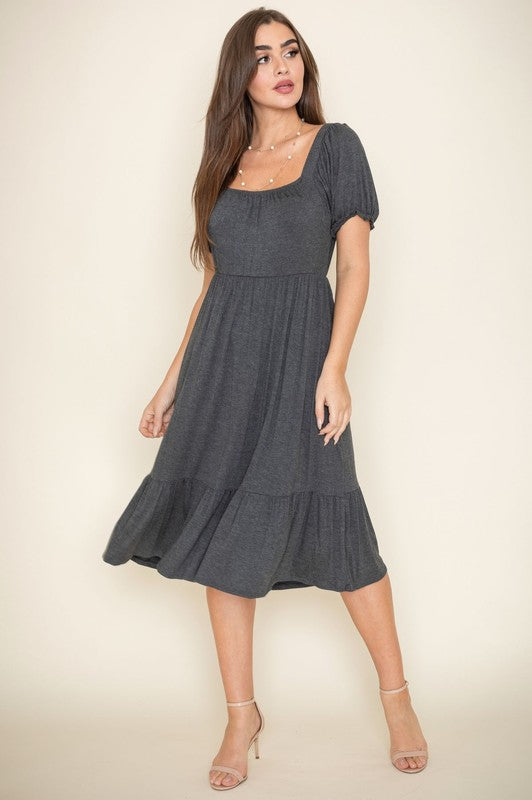 A woman in a Square Neck Puff Sleeve Boho Dress stands against a light background, smiling with her long hair down and wearing high heel sandals.