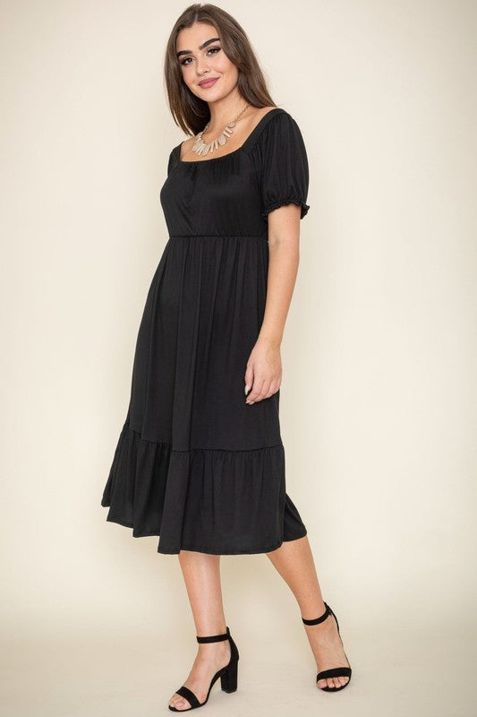 A woman in a Square Neck Puff Sleeve Boho Dress in light blue holds a wooden handbag. She stands on a plain background, wearing strappy heels.