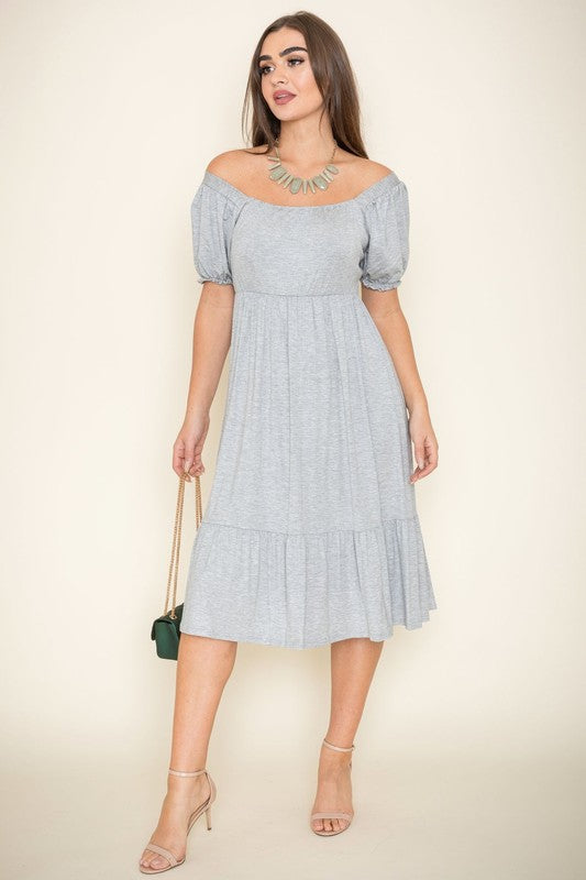 A woman in a Square Neck Puff Sleeve Boho Dress in light blue holds a wooden handbag. She stands on a plain background, wearing strappy heels.