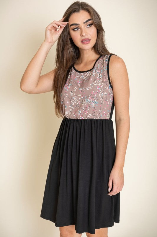 A woman wearing the Sleeveless Branch Floral Midi Dress with a vibrant top and black skirt is standing against a beige background.