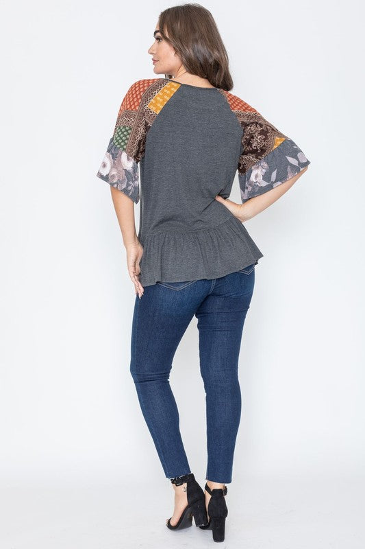 A woman wearing the Patchwork Ruffle Sleeve Tunic, featuring colorful patchwork sleeves, paired with blue jeans, stands against a plain background.