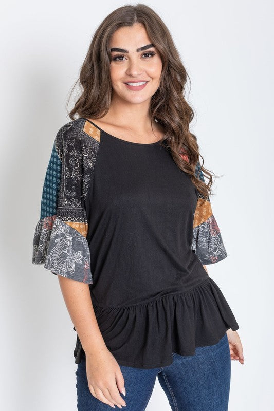 A woman wearing the Patchwork Ruffle Sleeve Tunic, featuring colorful patchwork sleeves, paired with blue jeans, stands against a plain background.