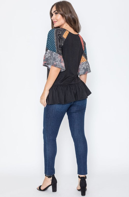 A woman wearing the Patchwork Ruffle Sleeve Tunic, featuring colorful patchwork sleeves, paired with blue jeans, stands against a plain background.