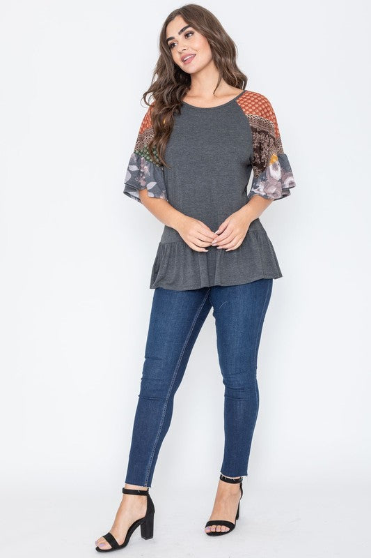 A woman wearing the Patchwork Ruffle Sleeve Tunic, featuring colorful patchwork sleeves, paired with blue jeans, stands against a plain background.