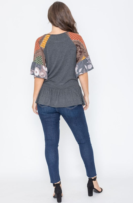A woman wearing the Patchwork Ruffle Sleeve Tunic, featuring colorful patchwork sleeves, paired with blue jeans, stands against a plain background.