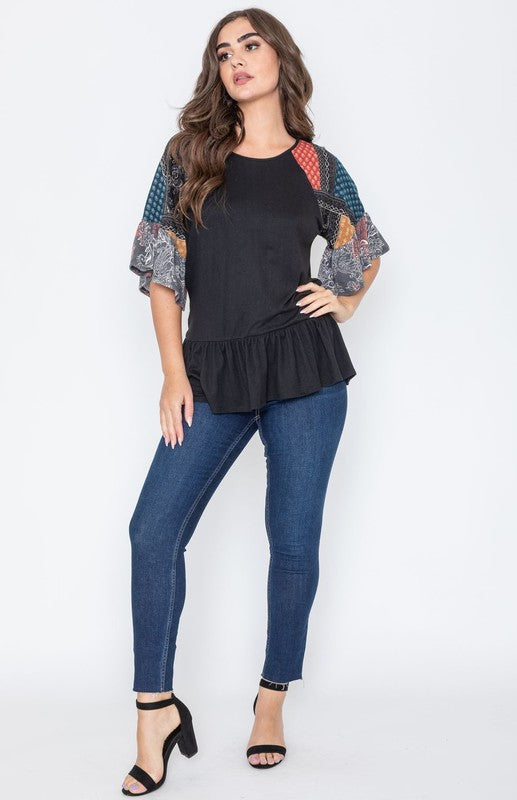 A woman wearing the Patchwork Ruffle Sleeve Tunic, featuring colorful patchwork sleeves, paired with blue jeans, stands against a plain background.