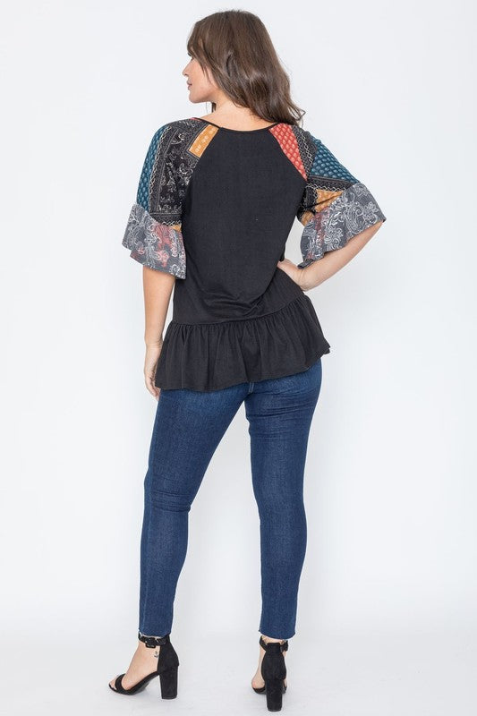 A woman wearing the Patchwork Ruffle Sleeve Tunic, featuring colorful patchwork sleeves, paired with blue jeans, stands against a plain background.