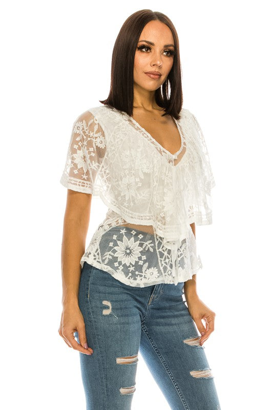 A person wearing a Lace White Top with a V neck and blue ripped jeans stands against a plain white background.