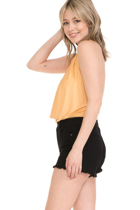 A person with long, light-colored hair wears the Sexy Top, a yellow draped halter in a solid pattern, paired with black denim shorts against a white background.