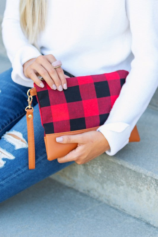 A person with long blonde hair holds the Buffalo Plaid Clutch, featuring a PU leather trim, while wearing blue jeans and a white sweater.