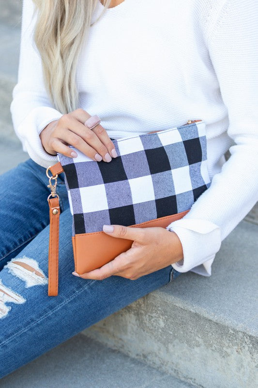 A person with long blonde hair holds the Buffalo Plaid Clutch, featuring a PU leather trim, while wearing blue jeans and a white sweater.