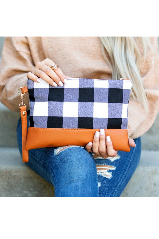 A person with long blonde hair holds the Buffalo Plaid Clutch, featuring a PU leather trim, while wearing blue jeans and a white sweater.