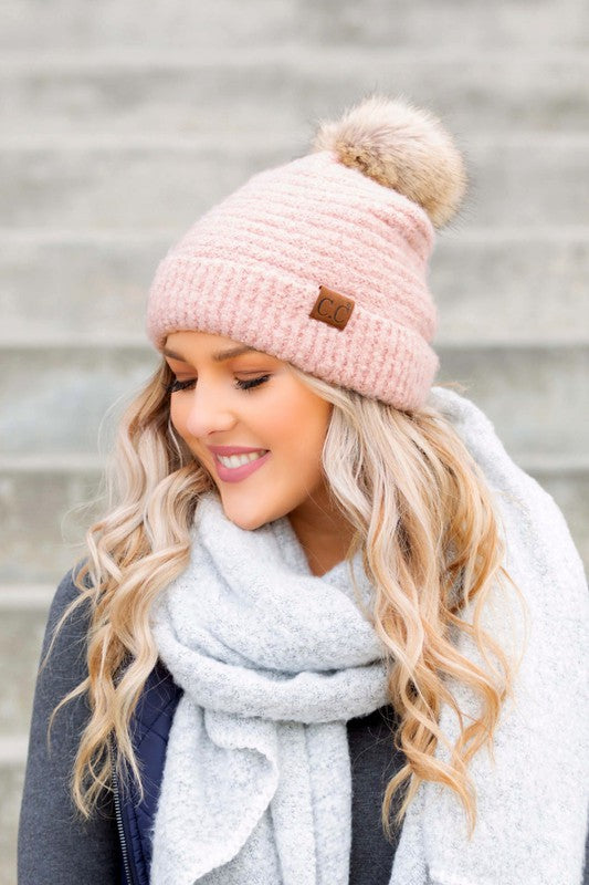 Woman wearing a grey CC Ultra Soft Fur Pom Beanie and a scarf smiling at the camera.