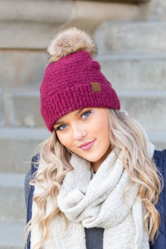 Woman wearing a CC Ultra Soft Fur Pom Beanie and a scarf, smiling at the camera.