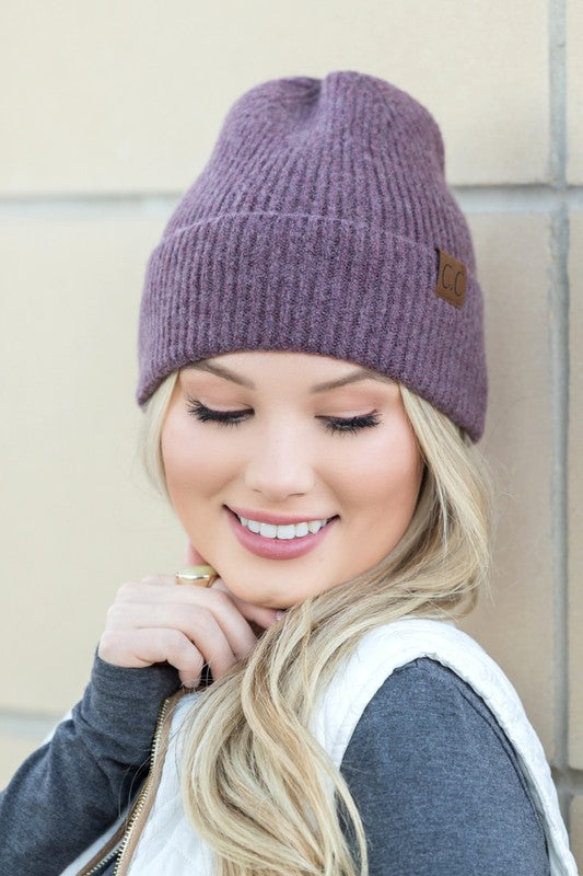 A smiling woman wearing a gray CC Fine Yarn Cuff Beanie boyfriend fit beanie with a brown leather logo patch.
