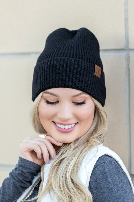 A smiling woman wearing a gray CC Fine Yarn Cuff Beanie boyfriend fit beanie with a brown leather logo patch.