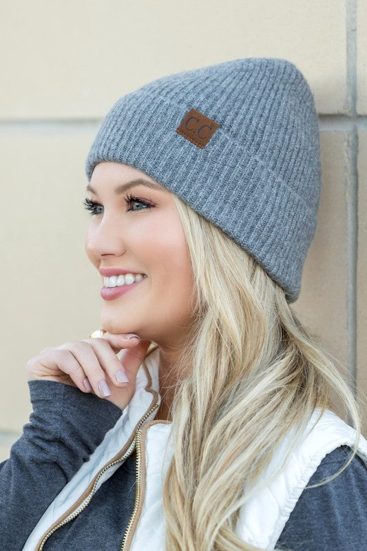 A smiling woman wearing a gray CC Fine Yarn Cuff Beanie boyfriend fit beanie with a brown leather logo patch.