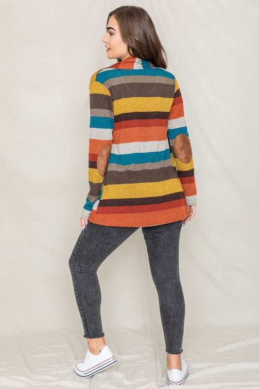 Dressed in a vibrant Stripe Elbow Patch Cardigan composed of soft spandex and polyester, paired with a white top and jeans, an individual stands against a light background.