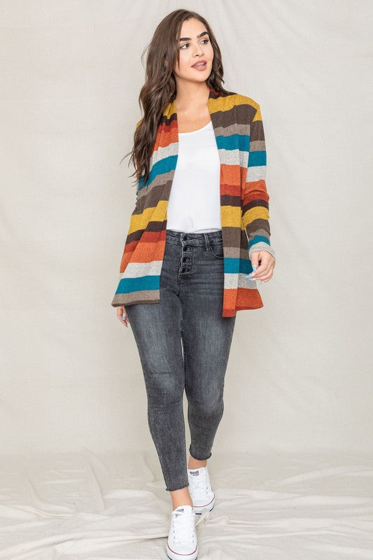 Dressed in a vibrant Stripe Elbow Patch Cardigan composed of soft spandex and polyester, paired with a white top and jeans, an individual stands against a light background.