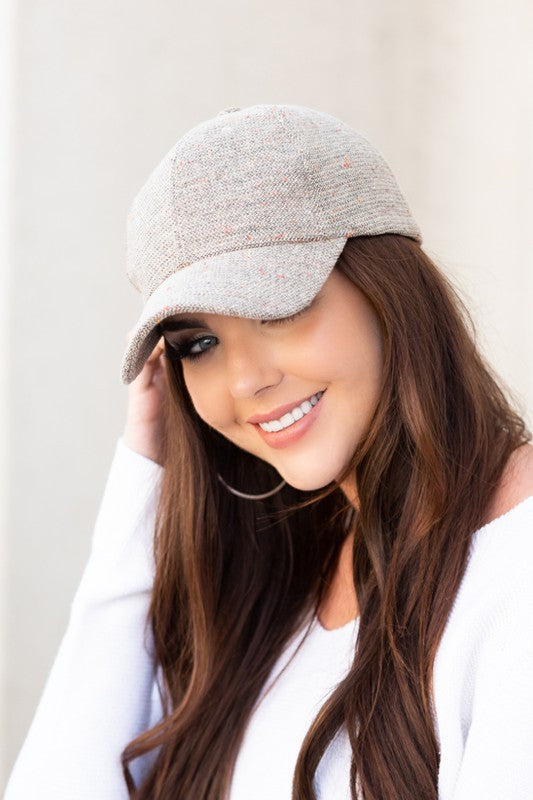 Woman smiling and wearing a Fall Tweed Ball Cap with an adjustable clasp and hoop earrings.