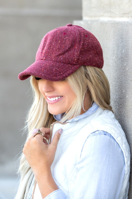 Woman smiling and wearing a Fall Tweed Ball Cap with an adjustable clasp and hoop earrings.