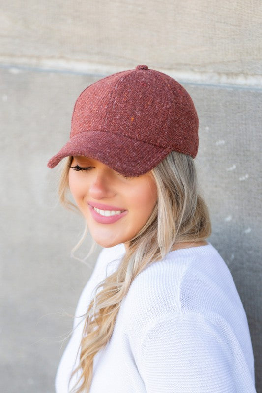 Woman smiling and wearing a Fall Tweed Ball Cap with an adjustable clasp and hoop earrings.