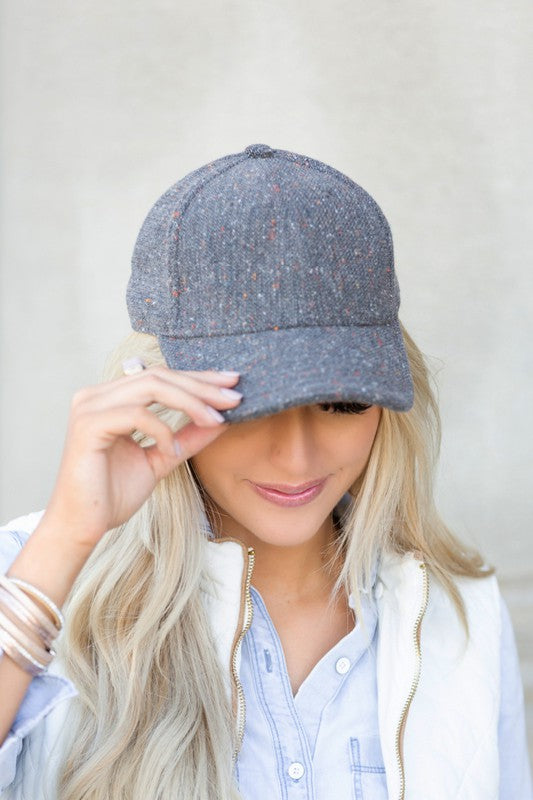 Woman smiling and wearing a Fall Tweed Ball Cap with an adjustable clasp and hoop earrings.