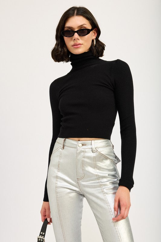 A size small model with short dark hair wearing black sunglasses, a TURTLE NECK LONG SLEEVE TOP in black, and metallic silver pants holds a small black handbag.