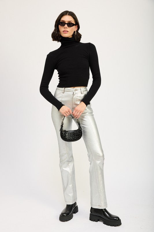 A size small model with short dark hair wearing black sunglasses, a TURTLE NECK LONG SLEEVE TOP in black, and metallic silver pants holds a small black handbag.