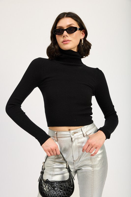 A size small model with short dark hair wearing black sunglasses, a TURTLE NECK LONG SLEEVE TOP in black, and metallic silver pants holds a small black handbag.