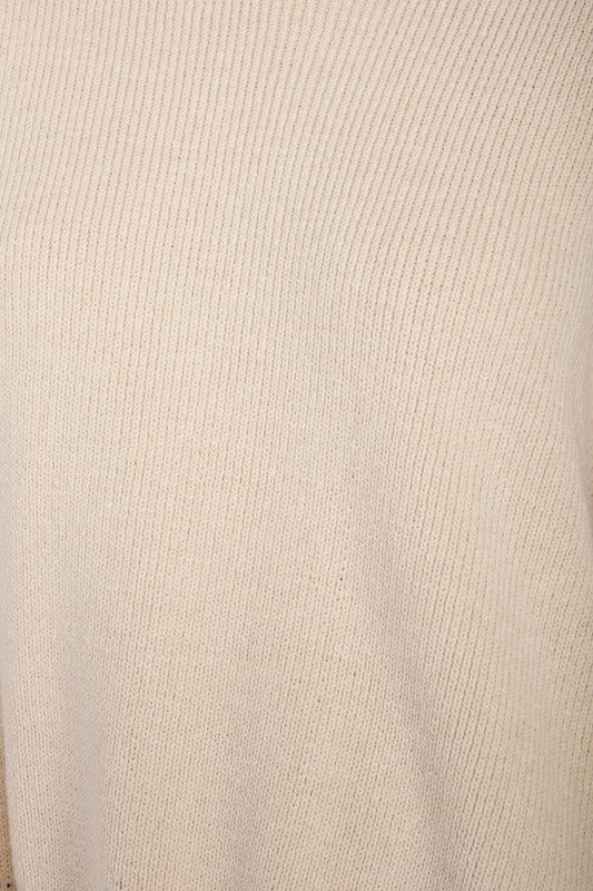 A woman wearing an OVER FITTED LONG SLEEVE SWEATER TOP made of 60% cotton in brown and khaki shorts holds a denim handbag with a brown strap against a neutral background.