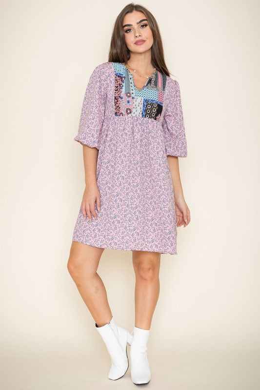 A woman wearing a 3/4 sleeve Ditsy Floral Patch Panel Boho Dress is standing gracefully in a room with a sofa in the background.