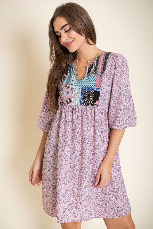 A woman wearing a 3/4 sleeve Ditsy Floral Patch Panel Boho Dress is standing gracefully in a room with a sofa in the background.