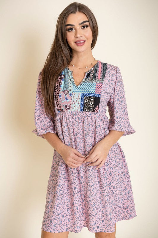 A woman wearing a 3/4 sleeve Ditsy Floral Patch Panel Boho Dress is standing gracefully in a room with a sofa in the background.