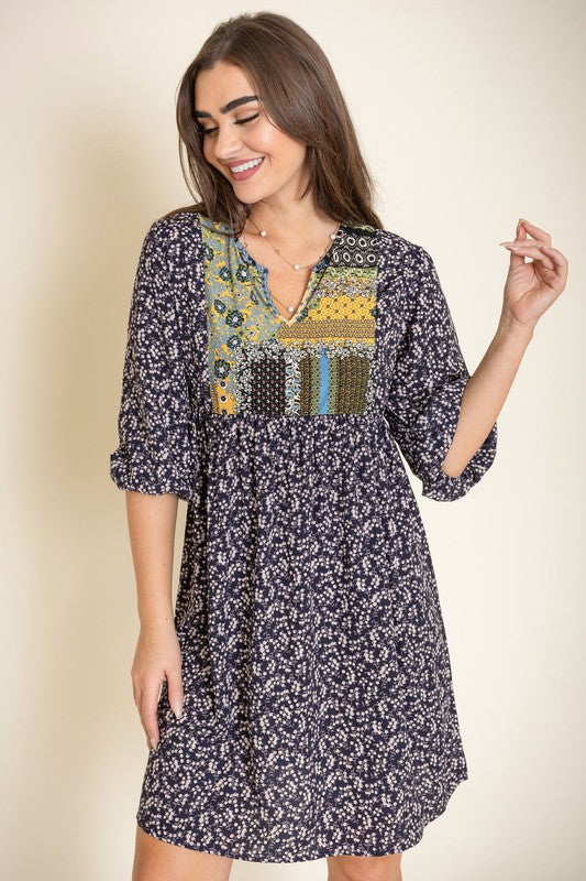 A woman wearing a 3/4 sleeve Ditsy Floral Patch Panel Boho Dress is standing gracefully in a room with a sofa in the background.