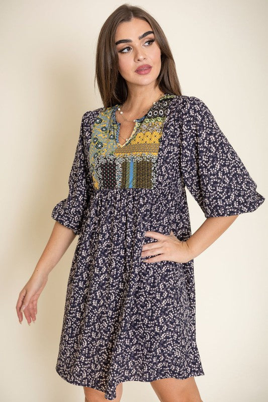 A woman wearing a 3/4 sleeve Ditsy Floral Patch Panel Boho Dress is standing gracefully in a room with a sofa in the background.