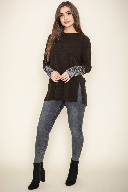 A person smiles with their eyes closed, wearing the Knit Side Slit Paisley Cuff Tunic in black, elegantly featuring paisley cuffs, with one hand touching their hair.