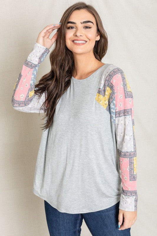 A woman wearing the Long Sleeve Patchwork Tunic in gray smiles with her eyes closed, standing against a light background.