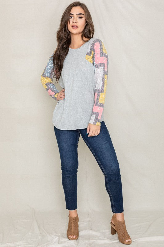 A woman wearing the Long Sleeve Patchwork Tunic in gray smiles with her eyes closed, standing against a light background.