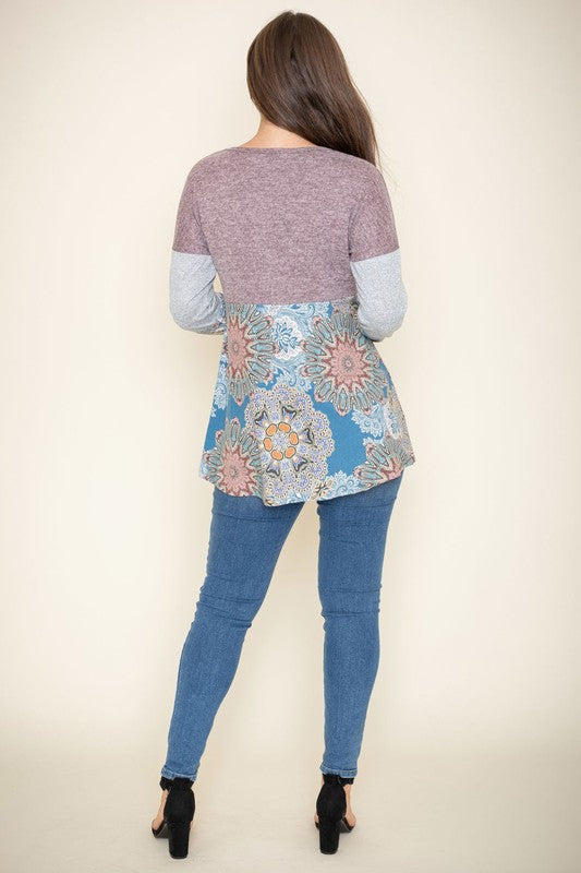 A person is wearing the Medallion Knit Color Block Tunic, crafted in the United States. It features intricate medallion knit details in shades of brown and gray, with a floral blue pattern adorning the bottom, and stands against a plain background.