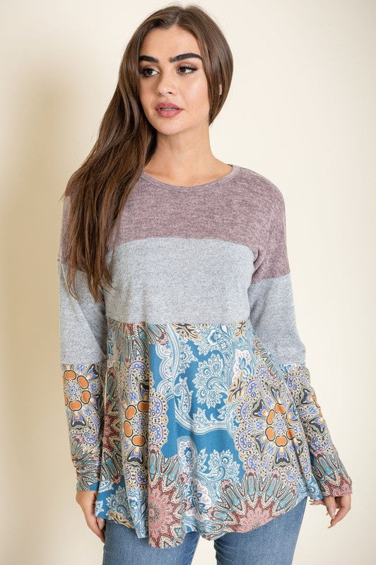 A person is wearing the Medallion Knit Color Block Tunic, crafted in the United States. It features intricate medallion knit details in shades of brown and gray, with a floral blue pattern adorning the bottom, and stands against a plain background.