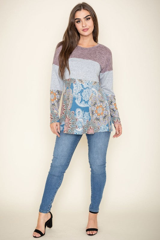 A person is wearing the Medallion Knit Color Block Tunic, crafted in the United States. It features intricate medallion knit details in shades of brown and gray, with a floral blue pattern adorning the bottom, and stands against a plain background.