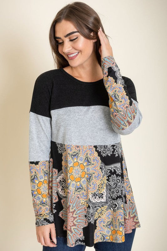 A person is wearing the Medallion Knit Color Block Tunic, crafted in the United States. It features intricate medallion knit details in shades of brown and gray, with a floral blue pattern adorning the bottom, and stands against a plain background.