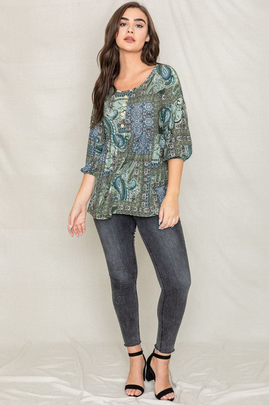 A woman with long brown hair wearing the Button Accent Paisley Top in green and blue, made from polyester, stands against a plain background.